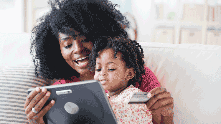 Woman reviewing balance transfer offers on her tablet with her daughter sitting in her lap